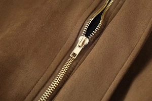 Macro detail of brown suede bomber jacket featuring a premium gold metal zipper