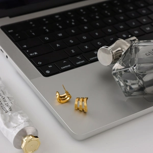 Détail de créoles triples couches plaquées or 18 carats sur fond de portable et de parfum