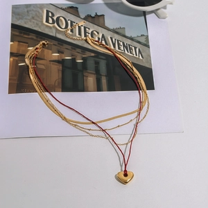 Macro detail of multi-layer gold heart pendant necklace with red cord and snake chain