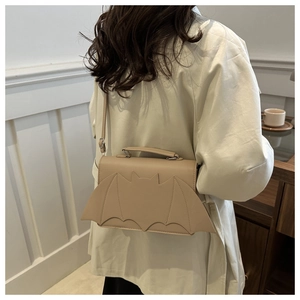 Model wearing a beige bat-shaped crossbody bag made of PU leather with metal buckle