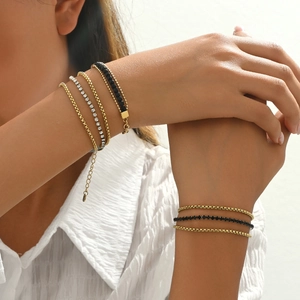 Close-up of layered stainless steel bracelets with gold chains and sparkling crystals