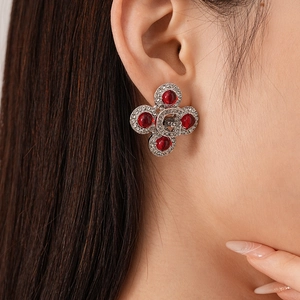 Detailed close-up of a vintage clover earring with red resin and G-letter on female model