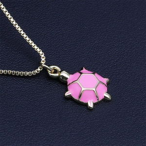 Nahaufnahme der goldenen Schildkrötenhalskette mit rosa Emaille-Anhänger auf Blau