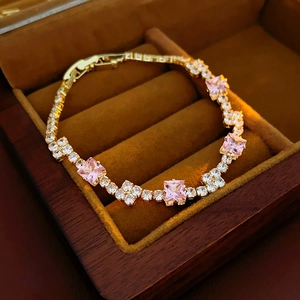 Close-up of pink square zircon and white round crystals on a gold chain bracelet