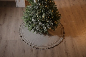 Detailed view of beige knitted Christmas tree skirt with fringes on wooden floor