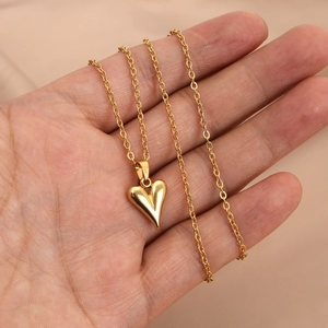 Polished gold heart pendant necklace on a delicate O-chain held in hand for scale
