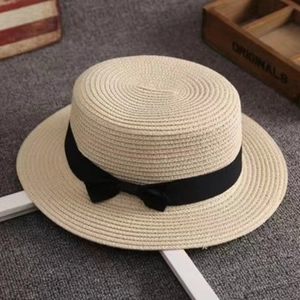 Detail of beige straw boater hat with a black ribbon bow on a gray textured rug