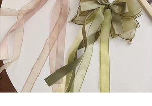 Macro detail of oversized olive green organza bow clip with delicate white pearl pendants