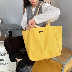 Detailed view of bright yellow large capacity canvas tote bag worn by a model indoors