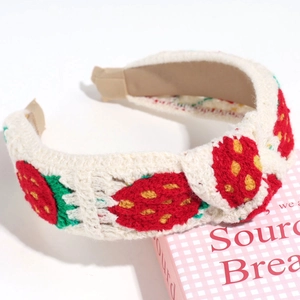 Close-up of hand-knitted beige headband featuring detailed red strawberry embroidery