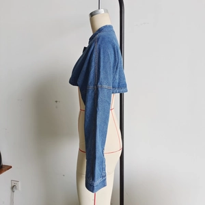 Detail view of the side profile of a cropped denim jacket on a mannequin in washed blue