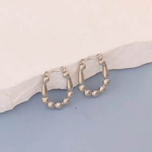 Macro detail of silver horseshoe earrings with textured beads on a stone background