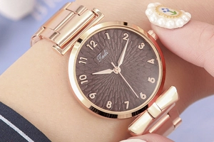 Detailed macro shot of rose gold watch dial featuring bow-shaped metal lugs and Tadi logo