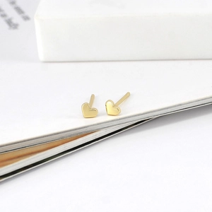 Macro shot of minimalist gold heart stud earrings resting on a white book page