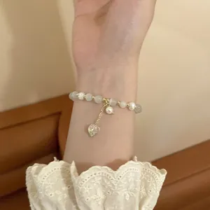 Detalle de pulsera de perlas y cuentas doradas con un colgante de corazón transparente