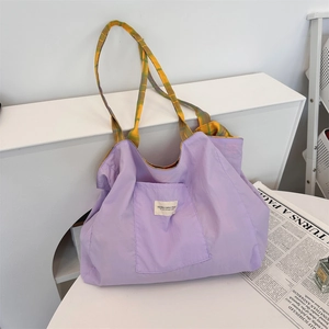 Détail du cabas en nylon violet avec étiquette blanche et bandoulière à carreaux