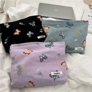 Flat lay of cotton cosmetic bags with butterfly floral embroidery beside a laptop