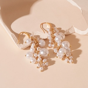 Macro shot of gold tassel earrings with varied white imitation pearls on textured stone