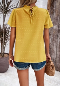 Detail of yellow high neck top featuring back tie ribbon and textured dot fabric