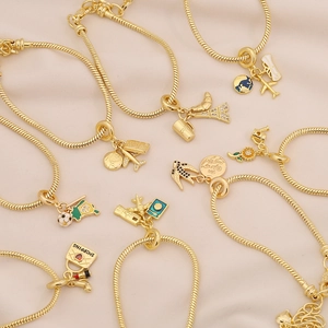 Gold snake chain bracelet with travel-themed charms like Eiffel Tower and globe on silk