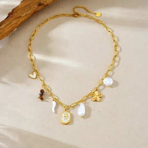 Detailed view of gold chain necklace with baroque pearls and heart pendants on sand