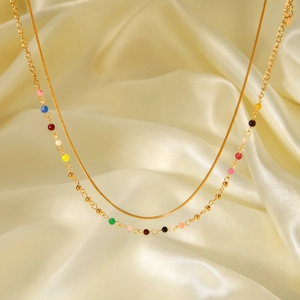 Detailed close-up of a double-layer gold beaded necklace on golden silk fabric background