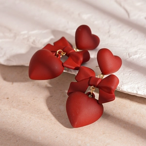 Detail of red bow and heart drop earrings with a matte finish and golden links