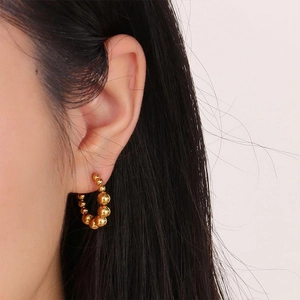 Close-up of gold beaded C-hoop earrings on model showing mirror metallic luster