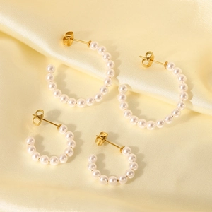 Detail view of large and small C-shaped pearl earrings on a soft satin fabric background