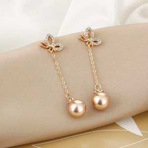 Close-up of golden tassel earrings with rhinestone butterfly studs and champagne pearl drops