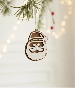 Close-up of a wooden Santa Claus ornament hanging on a pine branch with warm bokeh