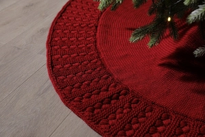 Close-up of red knitted Christmas tree skirt with cable stitch pattern on wood floor