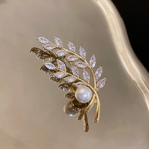 Close-up of gold wheat ear brooch featuring sparkling zircon stones and a pearl inlay