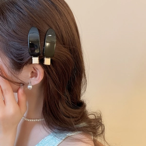 Glossy black oval hair clips worn on brown curly hair for a stylish side hairstyle