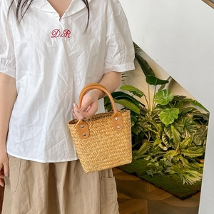 Close-up of minimalist straw tote bag with brown leather handles and silver studs detail
