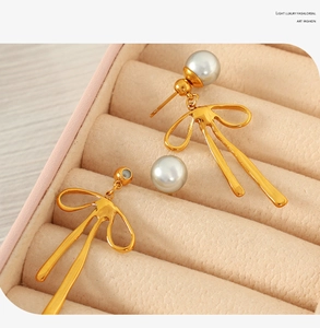 Detailed view of gold bow pearl earrings displayed in a soft pink velvet jewelry box