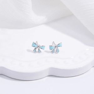Close-up of light blue ribbon stud earrings on a white wavy ceramic tray