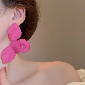 Close-up of large matte pink flower petal earrings on a model with soft lighting