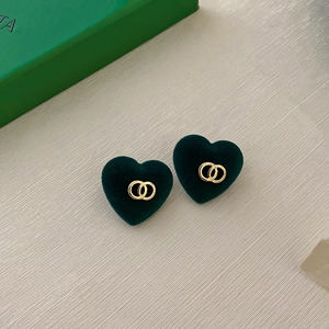 Detail of dark green heart stud earrings with golden interlaced rings on textured background