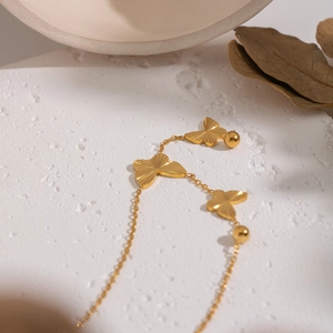 Detailed close-up of golden butterfly necklace with metallic beads on white stone