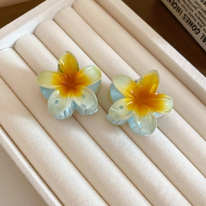 Close-up of two floral claw clips with gradient petals on a beige jewelry display tray