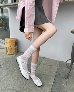 Close-up of white slouch socks paired with silk ballet flats and bow detail in a cafe setting