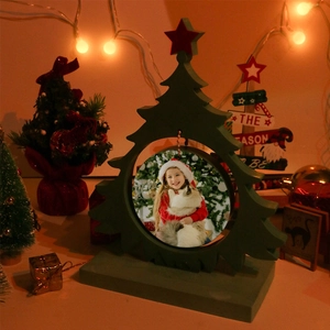 Close-up of a green wooden Christmas tree photo frame with a round cutout on a warm desk