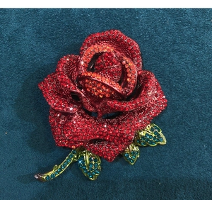Macro shot of rose brooch with red crystals and bronze finish on teal velvet