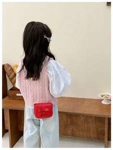 Detail showing a girl wearing a red mini crossbody bag with bow and golden chain