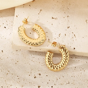 Close-up of golden C-shape earrings with hammered fish scale texture on stone background