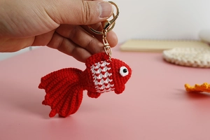 Close-up of handmade red crochet goldfish keychain with detailed knit texture