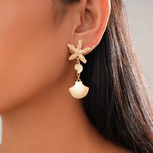Detail of model wearing gold starfish and seashell drop earrings with textured finish