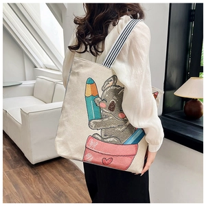 Lifestyle shot of an off-white canvas tote bag with a cartoon koala print and striped straps