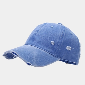 Dettaglio ravvicinato del berretto da baseball in denim blu lavato con tesa strappata e frange